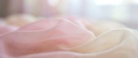 Soft flowing pink and cream silk fabric with gentle waves creating elegant textile background for luxury fashion and wedding design projects.