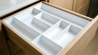White plastic cutlery tray organizer insert in open wooden kitchen drawer with compartments for utensils and silverware storage solution.