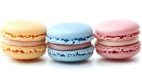 Colorful French macarons in pastel yellow, blue and pink flavors arranged on white background for bakery menu design and sweet dessert advertising.