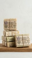 Stacked organic artisan soap bars with lavender and chamomile, wrapped in kraft paper with botanical illustrations, displayed on wooden surface for natural skincare and wellness product marketing.