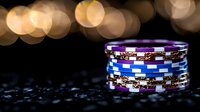 Casino poker chips stacked on dark surface with golden bokeh lights in background, creating luxurious gambling atmosphere for gaming and entertainment industry.