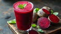 Fresh beetroot juice in glass with mint garnish and sliced beets on wooden board, healthy detox drink for wellness and nutrition lifestyle.