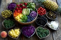 Colorful assortment of fresh fruits and vegetables in wooden bowls on rustic table, including berries, pineapple, cabbage, and greens for healthy eating.