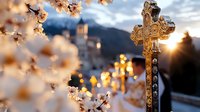 Ornate stone cross silhouetted against sunset sky with blooming cherry blossoms in foreground. Church spire and mountain landscape create spiritual atmosphere.