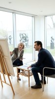 Professional mature businesswoman presenting strategy on easel to male colleague in modern office meeting room with large windows.