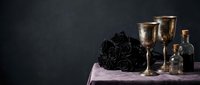 Gothic still life with black roses, antique brass goblets and glass bottles on purple velvet cloth against dark textured background for luxury design.