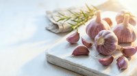 Fresh garlic cloves and whole bulbs with rosemary sprigs arranged on a marble cutting board, ideal for cooking, recipe, and food styling projects.