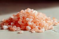 Pink Himalayan salt crystals in pile on light surface, macro shot showing mineral texture and natural pink hues for culinary and wellness concepts.