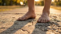 Barefoot male runner standing on asphalt road during golden hour, showcasing athletic feet and leg muscles for fitness, wellness, and outdoor exercise concepts.