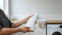 Empty toilet paper roll in hands of person in laundry room with washing machine, indicating need for replacement or household supplies.