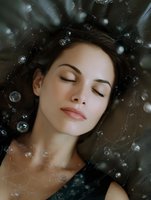 Young woman with closed eyes and serene expression lying surrounded by floating soap bubbles against dark background, creating dreamy atmospheric mood.