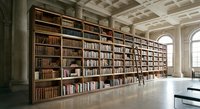 Grand library interior with floor-to-ceiling wooden bookshelves filled with books in elegant reading room with coffered ceiling and arched windows.