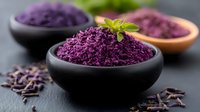 Purple cabbage powder in black ceramic bowls garnished with fresh herbs on dark background, raw organic superfood ingredient for healthy cooking.