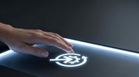Hand touching glowing cryptocurrency symbol on illuminated surface against dark background, representing digital finance and blockchain technology innovation.