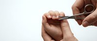 Hands using small scissors to trim fingernails in personal grooming routine. Clean manicure care and nail maintenance for hygiene and appearance.