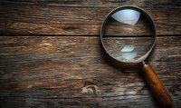 Vintage magnifying glass with wooden handle on rustic wooden background with dramatic lighting, creating mysterious detective atmosphere. Suitable for investigation concepts.