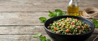 Fresh tabbouleh salad with parsley, tomatoes and bulgur in black bowl on rustic wooden table. Healthy Mediterranean cuisine for restaurant menus.