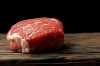 Fresh raw beef steak with white marbling on rustic wooden surface against dark background, close up view for food photography and culinary design.