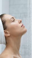 Woman with wet skin standing under flowing water stream, eyes closed in relaxation during shower or spa treatment for cleansing and wellness routines.