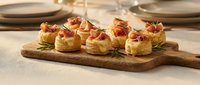 Gourmet puff pastry appetizers with prosciutto and herbs on wooden board, elegant party food presentation for catering and entertaining events.