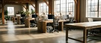 Modern open office workspace with wooden desks and ergonomic chairs in bright industrial loft with large windows and natural lighting for productivity.
