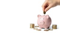 Hand dropping coin into pink piggy bank surrounded by stacked coins on white background for savings and financial planning concepts.