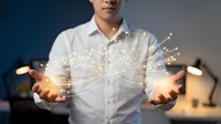 Young Asian businessman in white shirt holding glowing digital network connections with light trails emanating from hands in modern office setting.