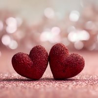 Two red glittery hearts on sparkling surface with soft bokeh background for Valentine's Day romance love celebration greeting cards wedding invitations.