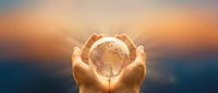 Hands gently holding glowing Earth globe against warm sunset sky, symbolizing environmental protection, global responsibility and planet care.