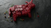 Raw beef cut in shape of bull or cow on dark stone background with herbs and spices, creative food art composition for steakhouse menu or butcher shop.