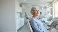 Senior Caucasian woman patient smiling confidently while sitting in modern dental office chair during routine checkup appointment with professional care.