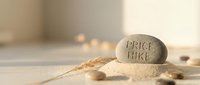 Engraved stone with price hike text surrounded by scattered pebbles and dried grass on neutral surface, symbolizing cost increase and inflation concerns.