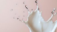 Dramatic milk splash crown shape with flying droplets on soft pink background, dynamic liquid motion captured in high speed photography.