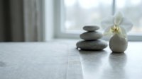 Stacked zen stones and white orchid flower on marble table by window, spa and wellness relaxation concept for meditation and mindfulness.