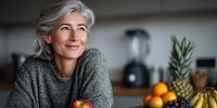 Mature woman with gray hair smiling in modern kitchen with fresh fruits, healthy lifestyle and nutrition concept for middle-aged adults.