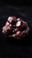 Raw red garnet crystal cluster specimen with natural faceted surfaces and deep crimson color on dark background for geology and mineral collection displays.