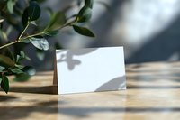 Blank white card with natural shadow and green leaves on wooden surface in sunlight, mockup for branding, wedding invitation or greeting card design.