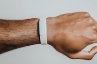 Male wrist wearing blank white silicone wristband against neutral background, showcasing minimalist accessory design for mockup and branding purposes.