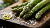 Fresh green asparagus spears on rustic wooden cutting board with sea salt and lemon zest for healthy cooking and gourmet meal preparation.