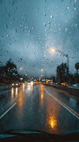 Raindrops on car windshield with blurred city lights and wet road at dusk, creating atmospheric mood for weather or travel concepts.