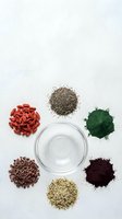 Nutritional supplements and superfoods arranged around empty glass bowl on white background. Goji berries, chia seeds, spirulina powder, cacao nibs, beetroot powder, hemp seeds isolated for wellness design.
