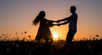 Romantic couple silhouettes holding hands dancing in wildflower meadow at golden sunset creating intimate moment for love and relationship concepts.