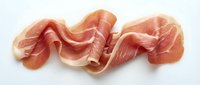 Thin slices of cured prosciutto ham isolated on white background, showing delicate pink marbling and soft folds of Italian dry-cured meat.