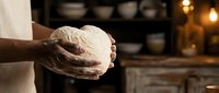 Baker hands holding fresh artisan bread dough in warm kitchen with bokeh lights creating cozy bakery atmosphere for culinary and food preparation concepts.