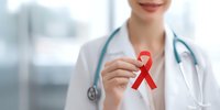 Female healthcare professional in white coat holding red AIDS awareness ribbon, promoting HIV prevention and support in medical setting.