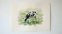 Watercolor painting of black and white spotted cow grazing in green pasture on white paper background for farmhouse decor and agricultural artwork.