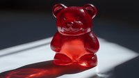 Red translucent gummy bear candy on white surface with dramatic lighting and shadow, popular sweet treat for children and adults.