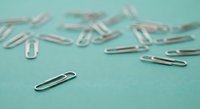 Silver metal paper clips scattered on mint green background for office supplies and business organization concepts.
