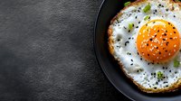 Fried egg with runny yolk and herbs in black pan on dark slate background. Fresh breakfast meal with seasoning and copy space for culinary designs.