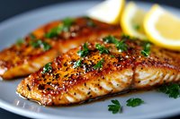 Grilled salmon fillet with honey glaze, black pepper crust and fresh herbs garnish on gray plate, served with lemon wedges. Close up of seafood dinner.